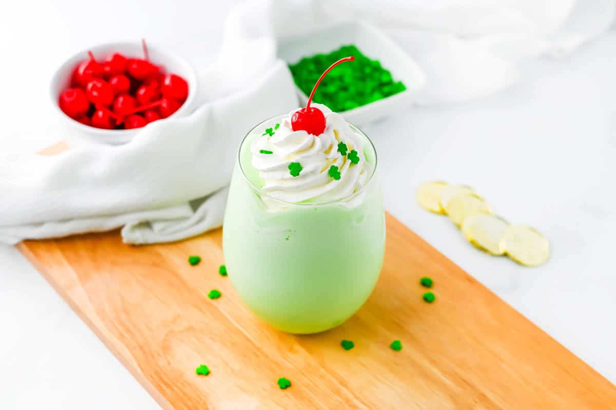 Shamrock shake on wood board with cherries and sprinkles in the background