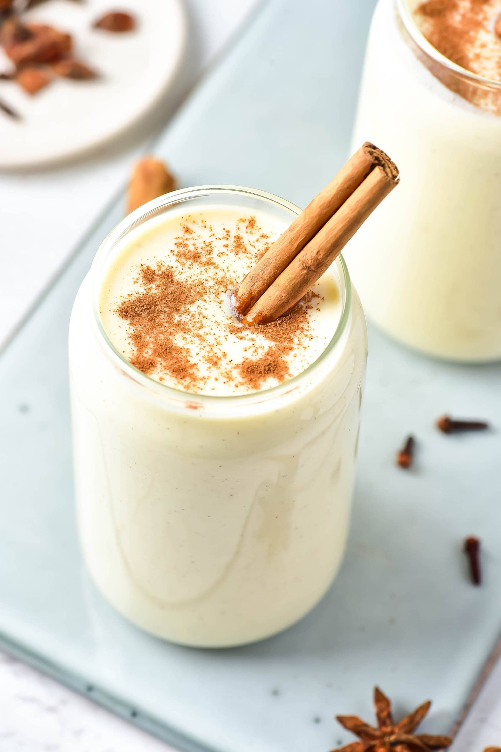 Eggnog protein shakes on glass counter with a little cinnamon on top and cinnamon sticks 