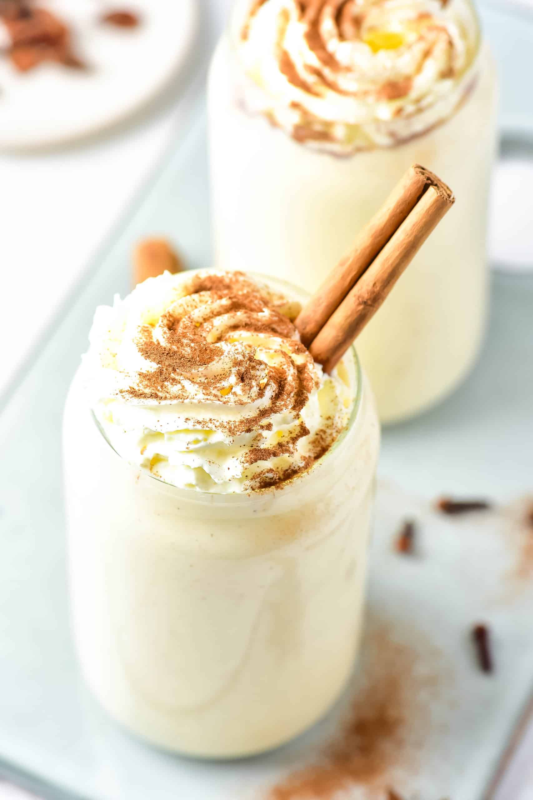Eggnog protein shake with whipped cream and cinnamon sticks.