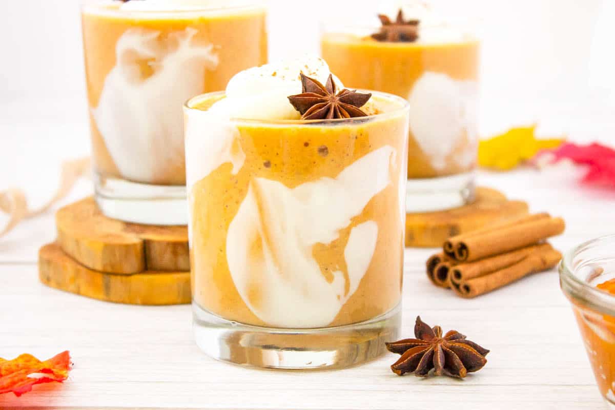 Three pumpkin pie smoothies with cinnamon sticks and allspice stars in the background.