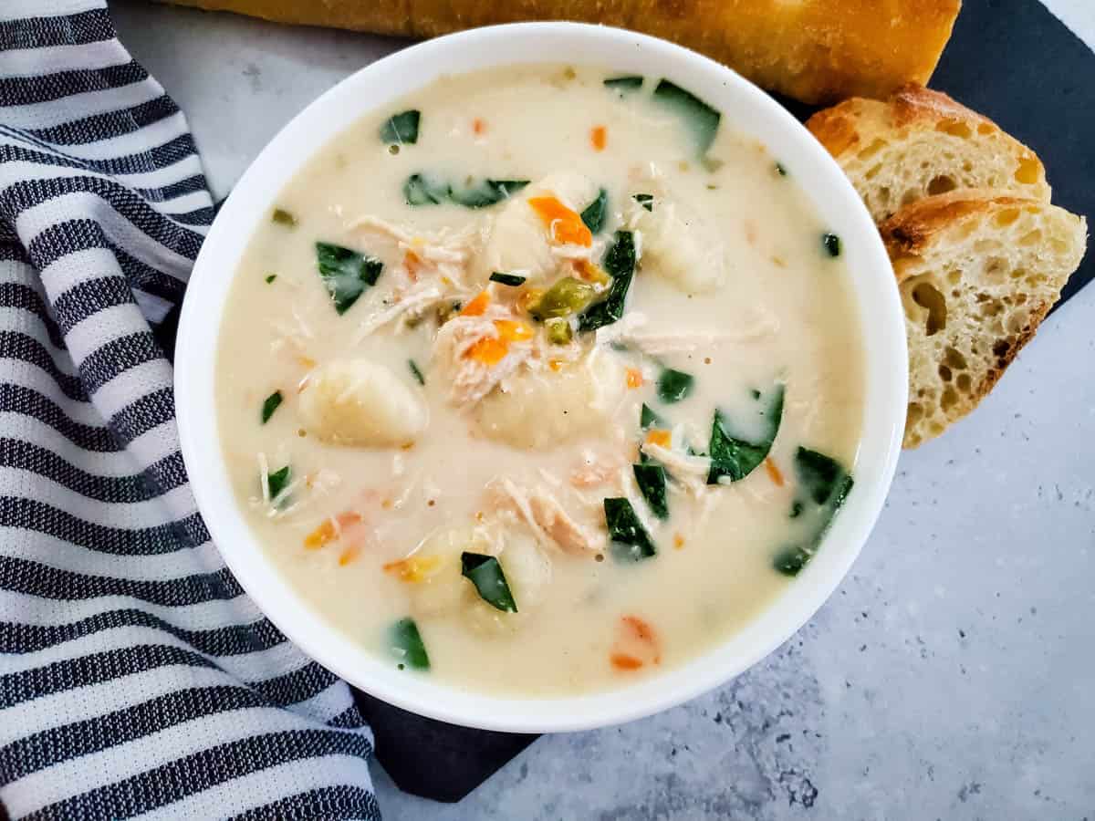 White bowl with soup next to blue and white strip towel with bread next to bowl