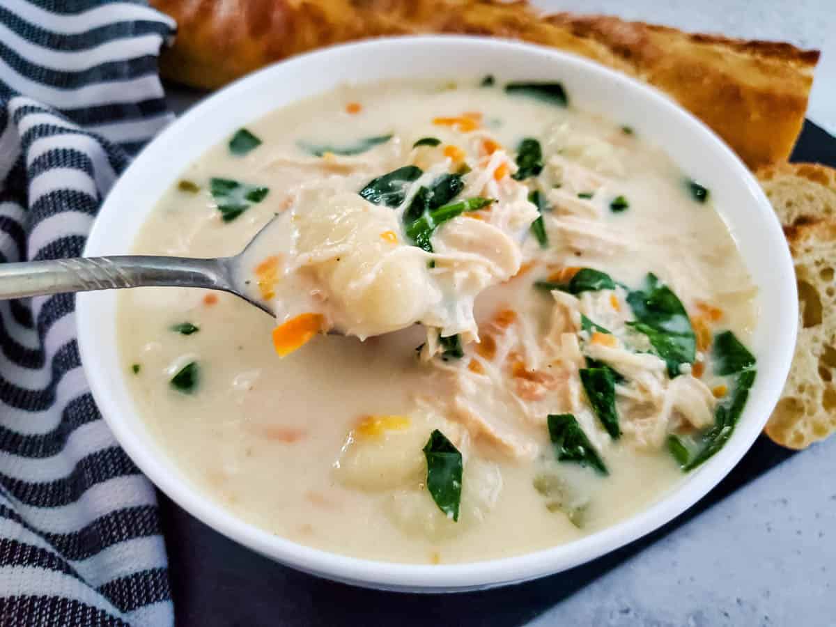 Bowl of creamy chicken gnocchi soup with soup lifting contents up. Blue and white strip towel next to bowl.