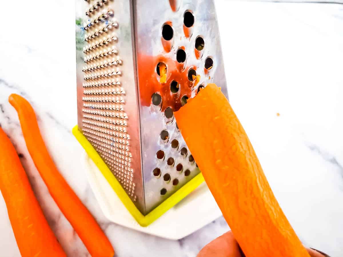 Single carrot being grated on a cheese grater.