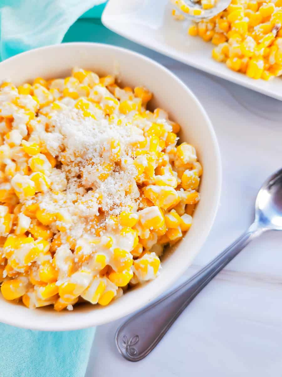 White bowl with mexican street corn with spoon on the side.