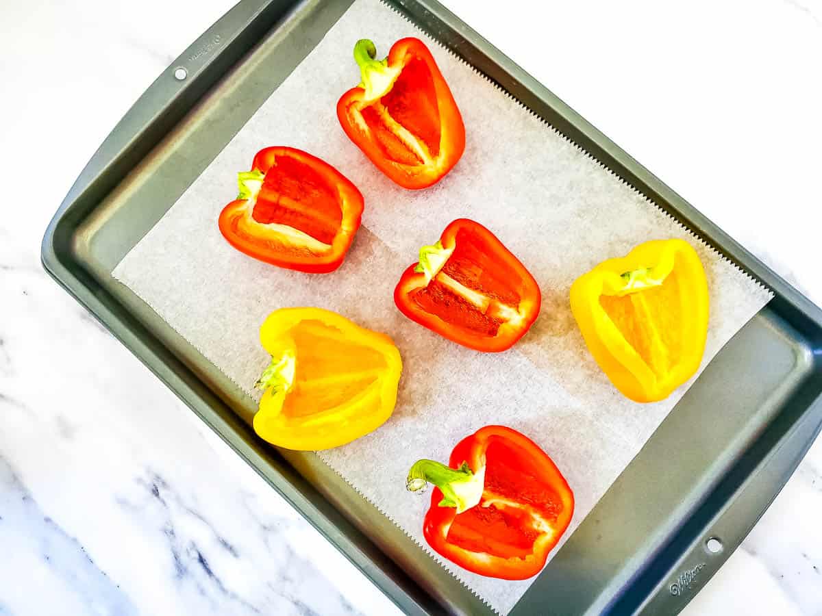 Peppers cut lengthwise on a tray covered in parchment paper.