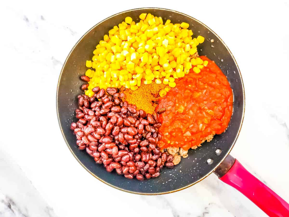 Skillet with black beans, taco seasoning, corn, salsa and meat on white background.