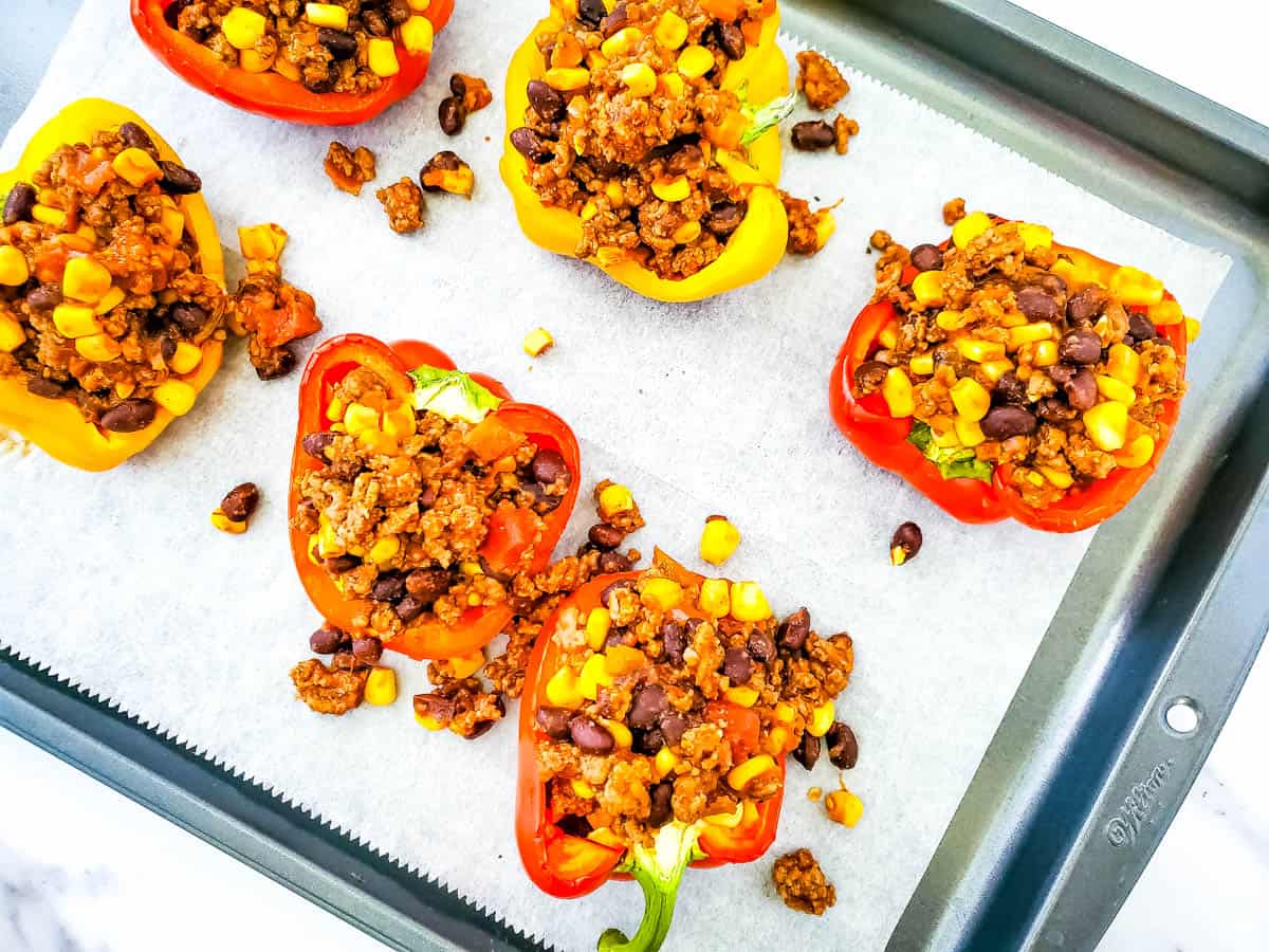 Baking sheet with parchment paper and peppers filled with taco mixture.