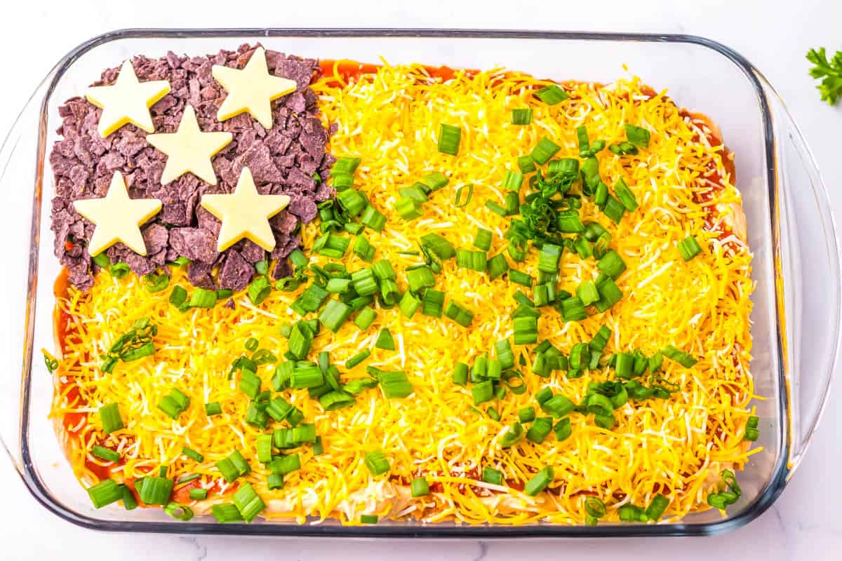 Taco dip with 5 white stars and crushed blue corn chips in corner of baking dish on top of layered dip