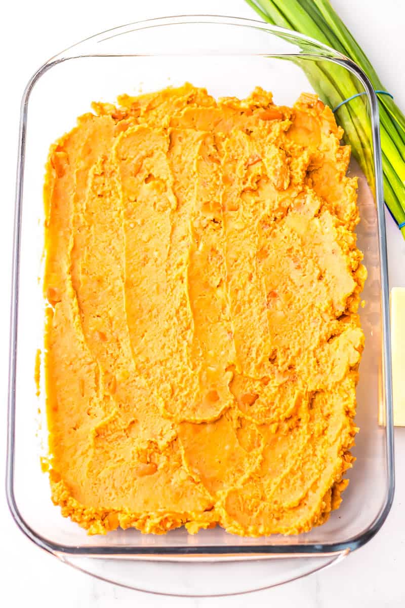 Baking dish with refried beans spread out on it.