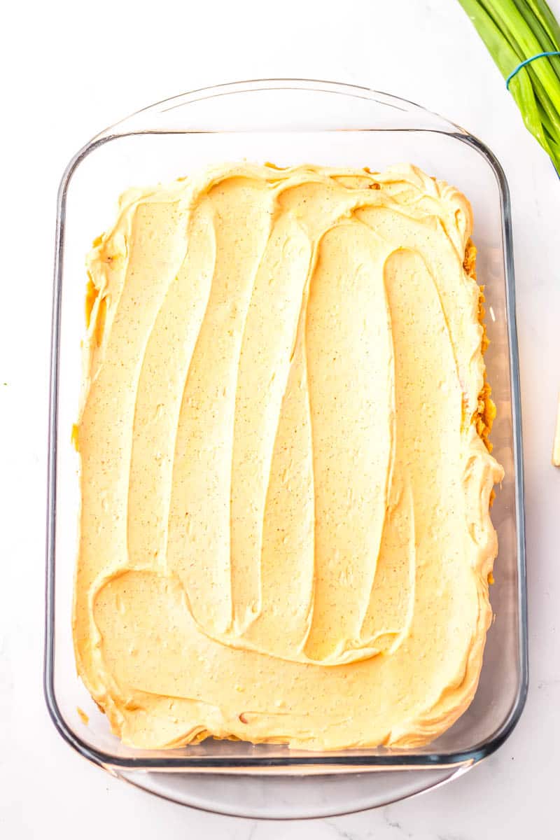 Sour cream and cream cheese and taco seasonings on top of refried beans in a baking dish