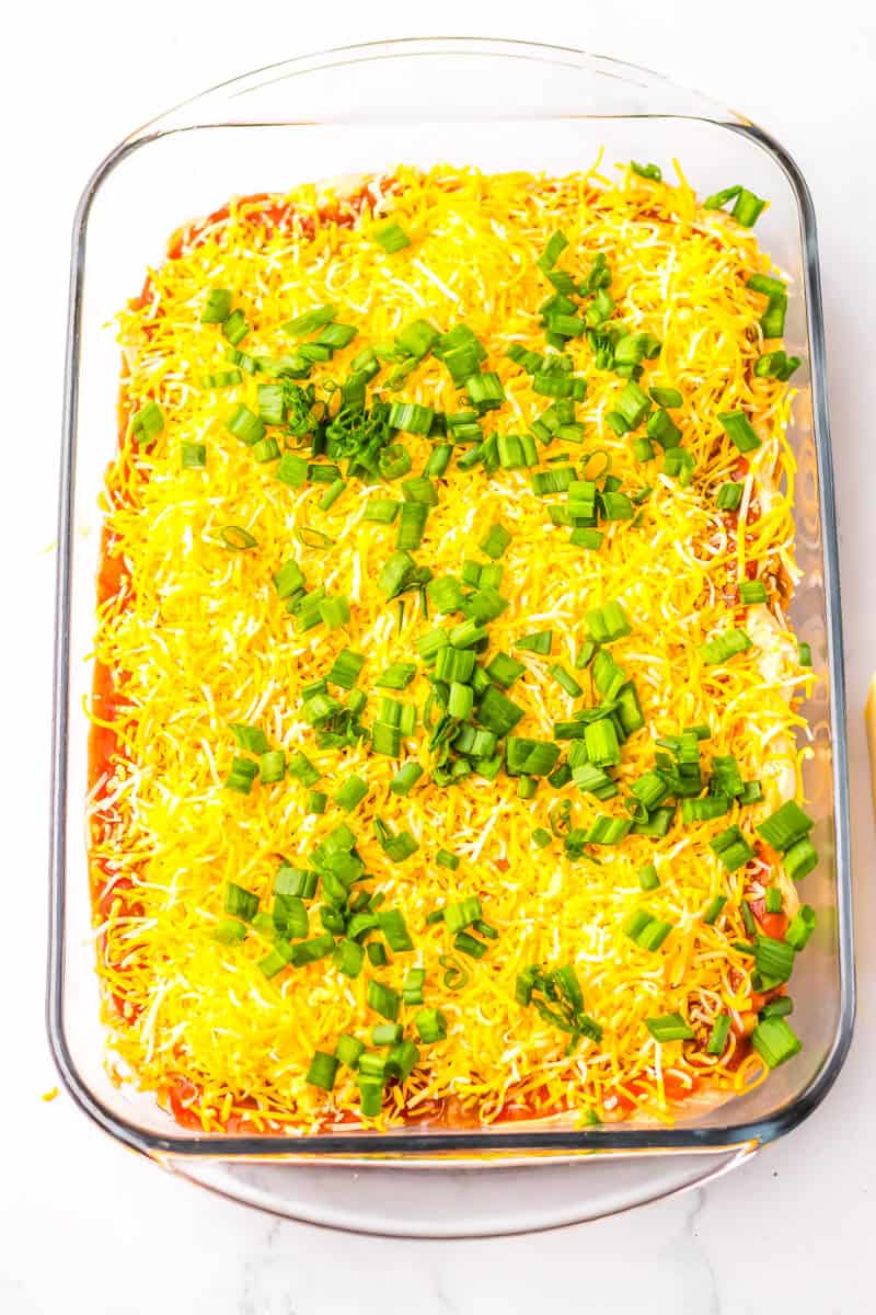 Shredded cheese and green onions on top of cream cheese mixture and refried beans in a baking dish