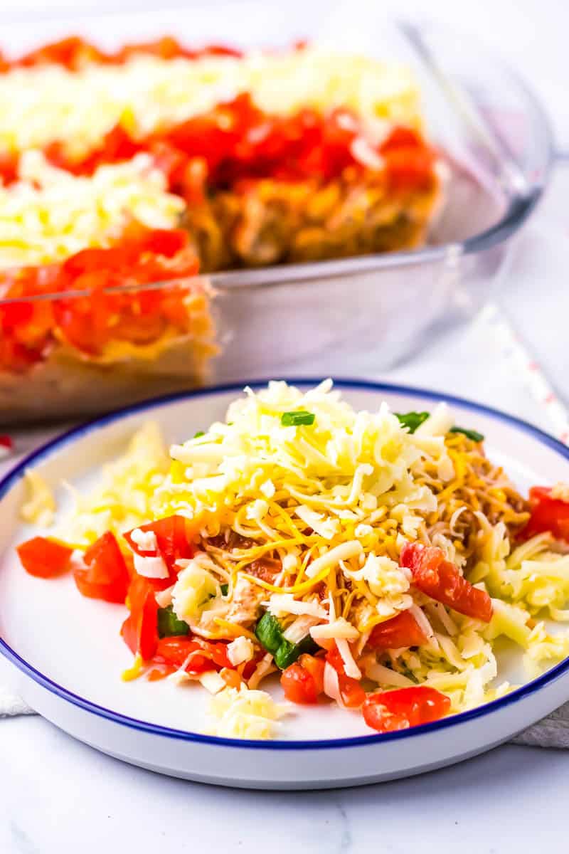Plated taco dip with the rest in the baking dish in the background on white surface.