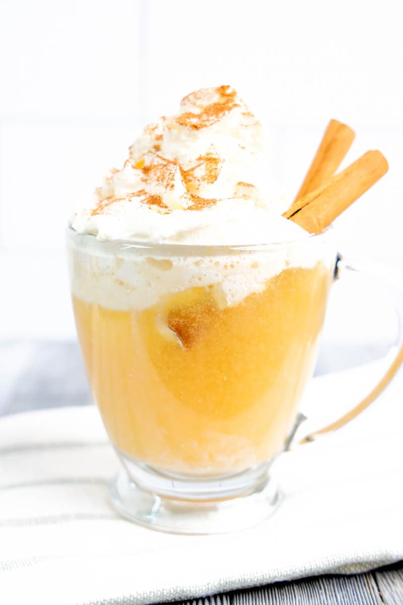 Apple cider float in clear glass cup on white towel with gray stripe. White and gray background