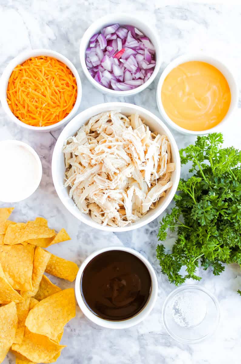 Individual ingredients for the bbq chicken nachos in bowls on a gray marble background.
