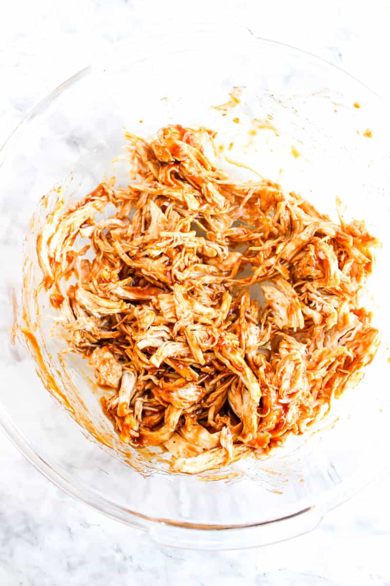Shredded chicken mixed with bbq sauce in a clear bowl.