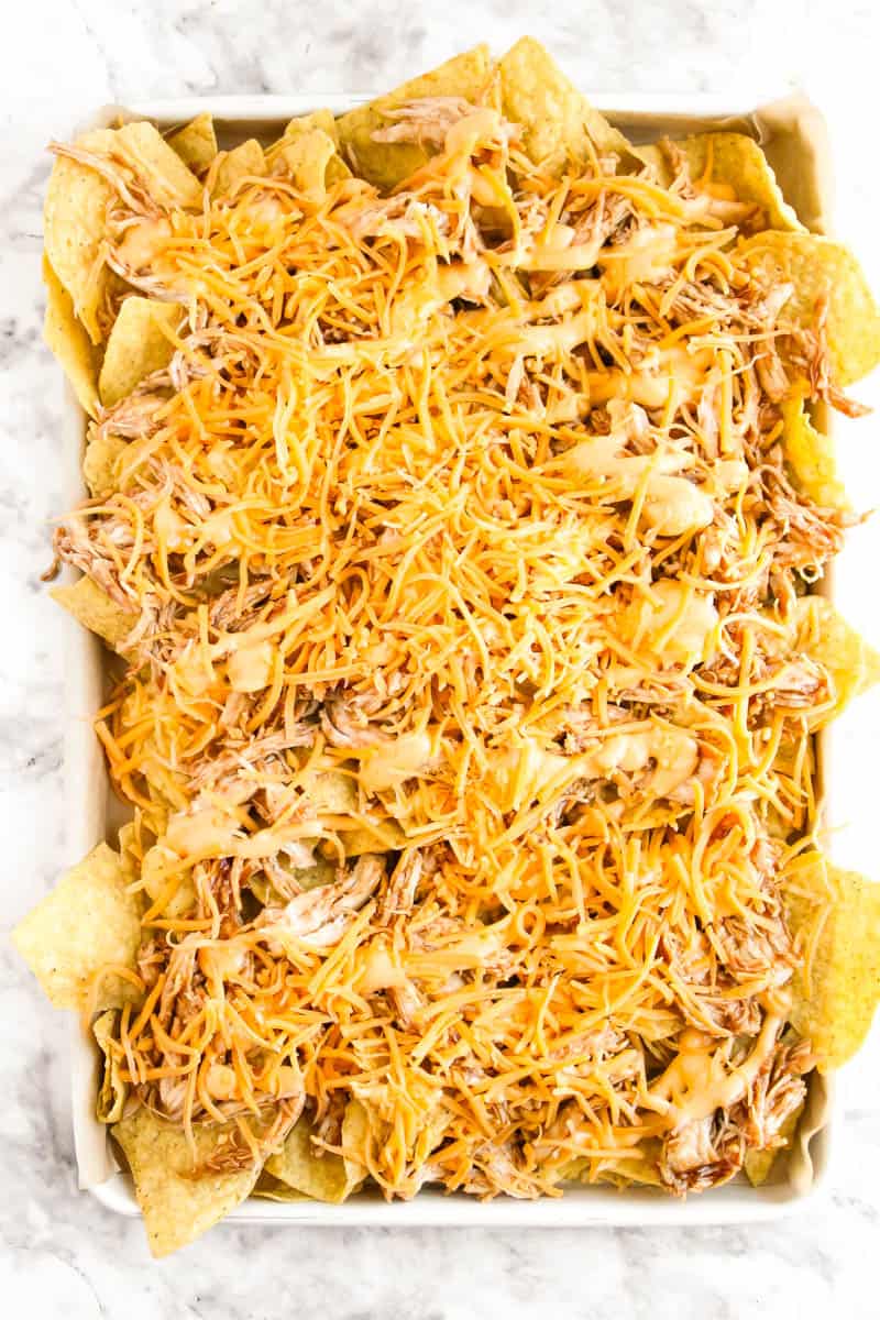 Layered nachos with chicken, bbq sauce and cheese on a sheet pan.