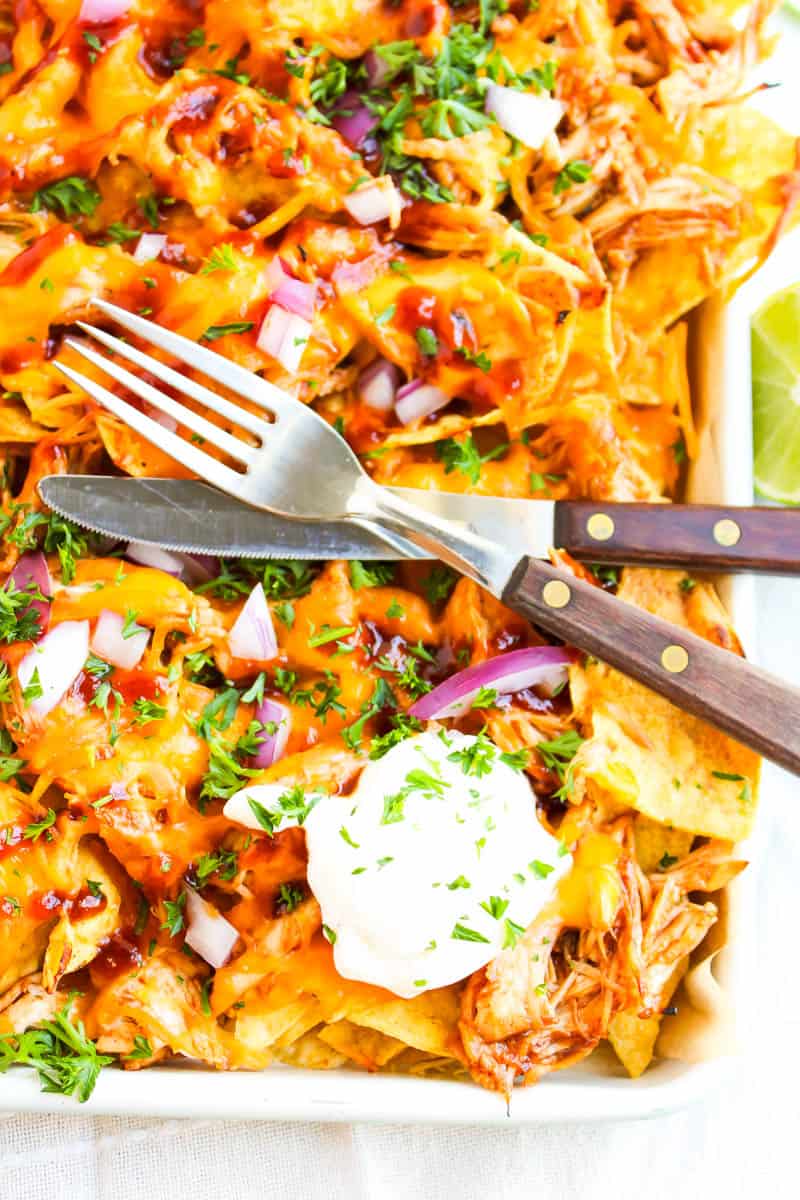 Bottom right corner of sheet pan bbq chicken nachos with fork and knife over the chips.