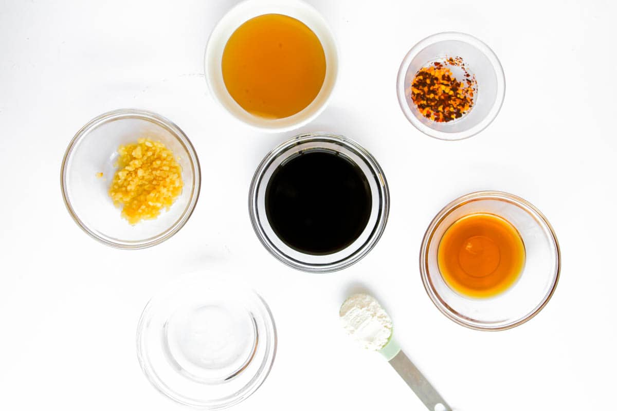 Ingredients for marinade in clean bowls-coconut aminos, minced garlic,  water, sesame oil, honey and red chili flakes. A tablespoon of arrowroot powder is also there.