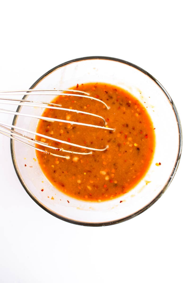 Clear bowl with marinade ingredients and whisk in it.
