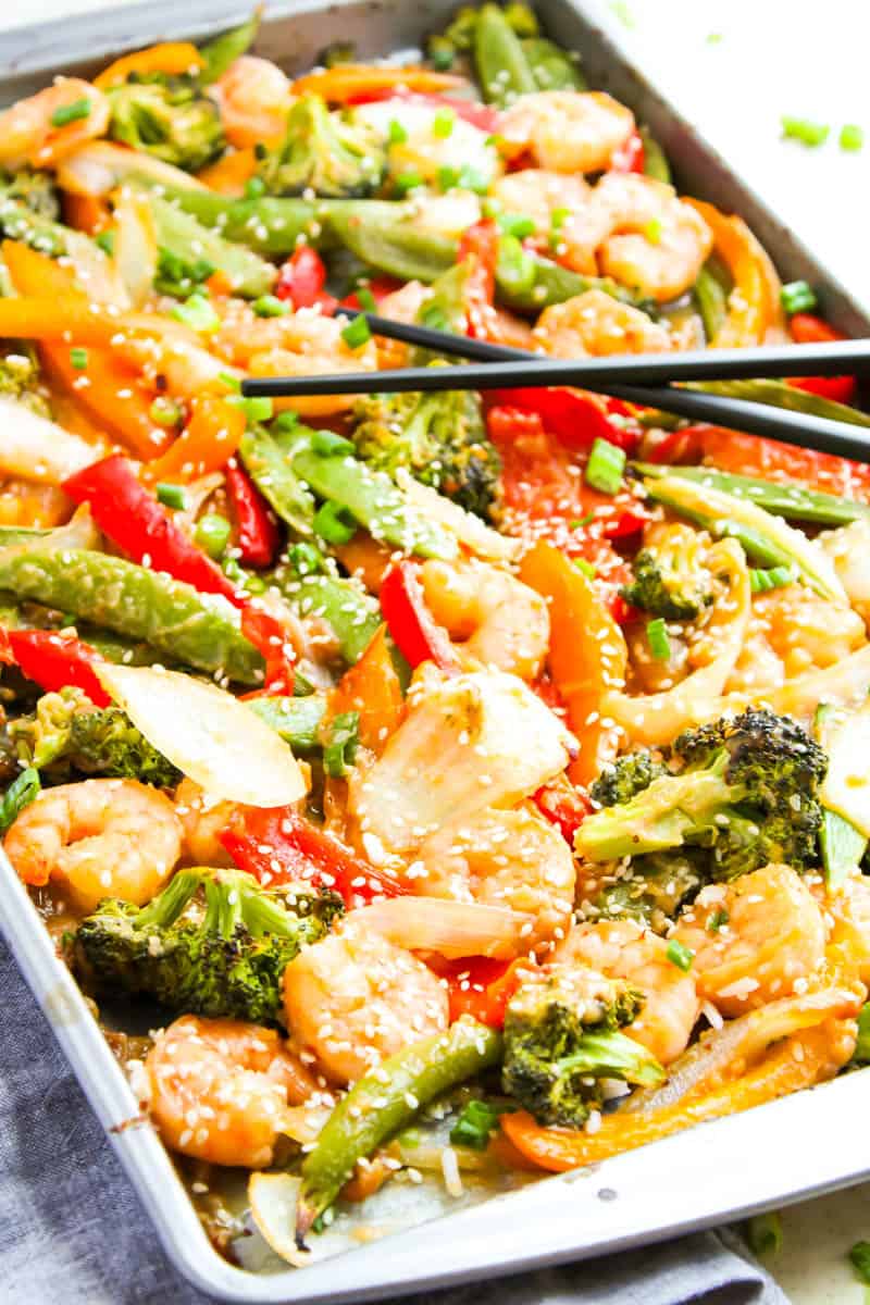 Sheet pan shrimp stir fry on pan with black chopsticks laying across pan.