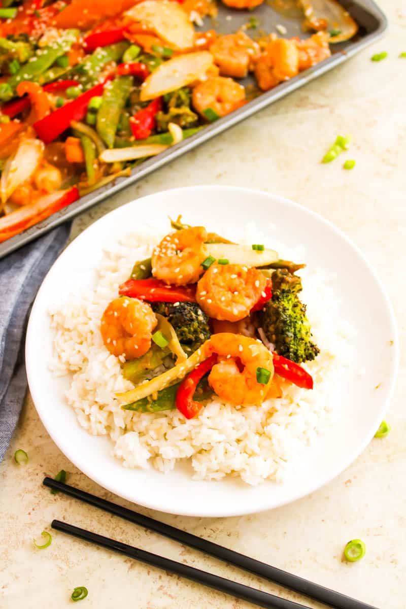 White plate with rice and shrimp stir fry on top. Sheet pan in the left corner on white background.
