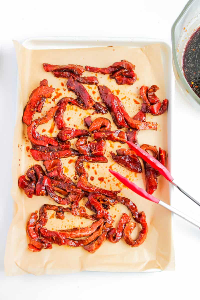 Pieces of steak being placed on sheet pan with tongs.