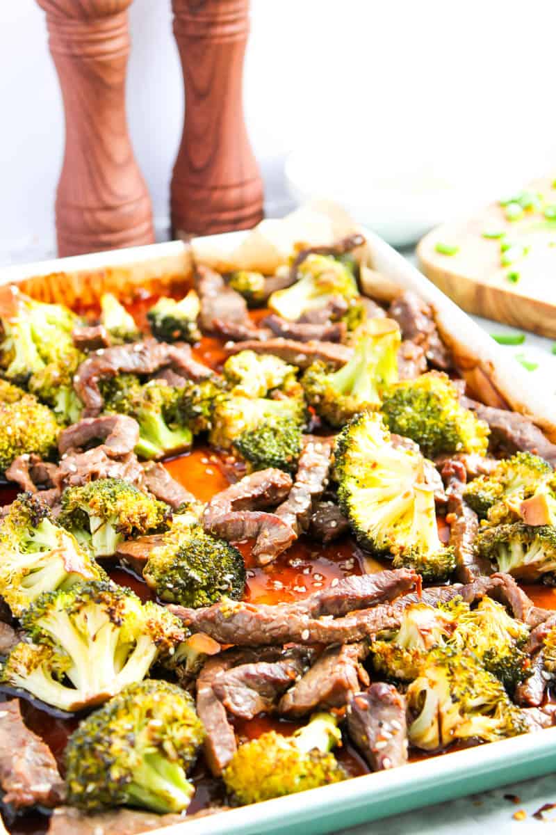 Close up of sheet pan with beef and broccoli on it and brown salt and pepper shakers in the background.