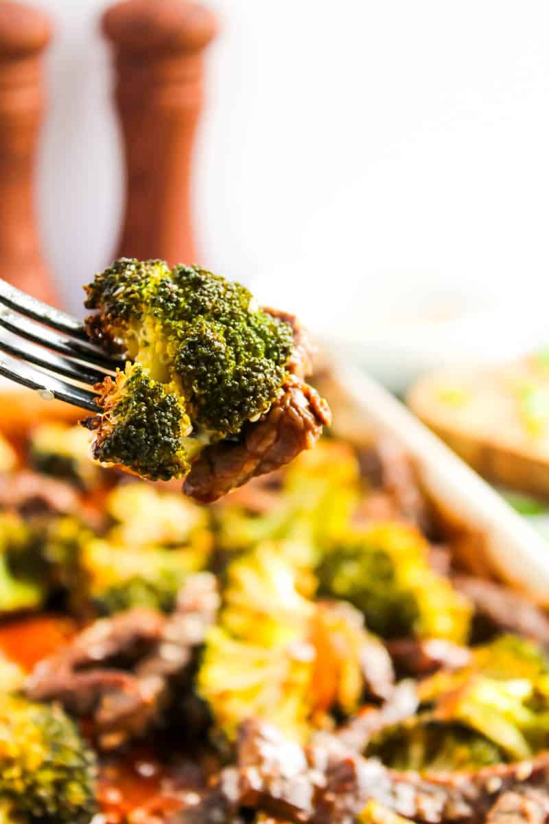 Close up of piece of broccoli on fork with sheet pan beef and broccoli in the background.