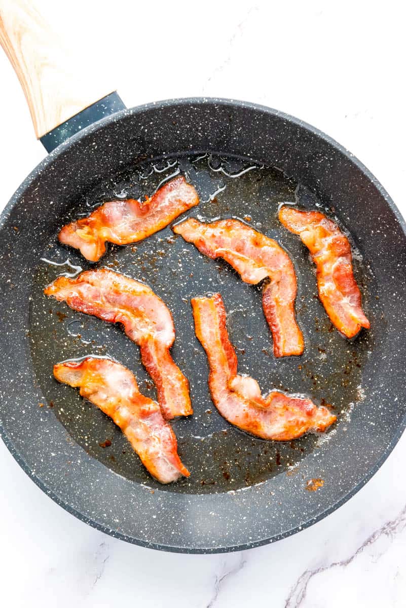 Six bacon slices in a gray frying pan on white background.