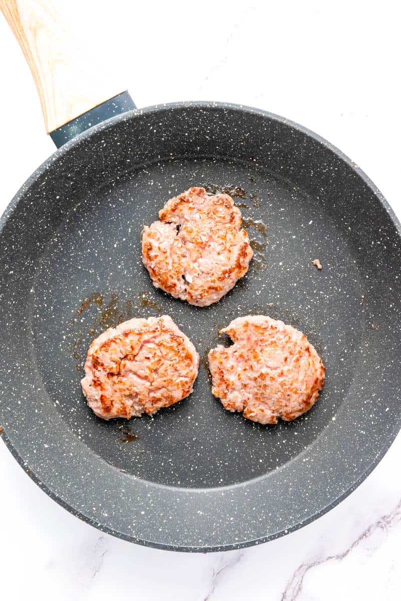Three sausage patties in gray frying pan on white background.