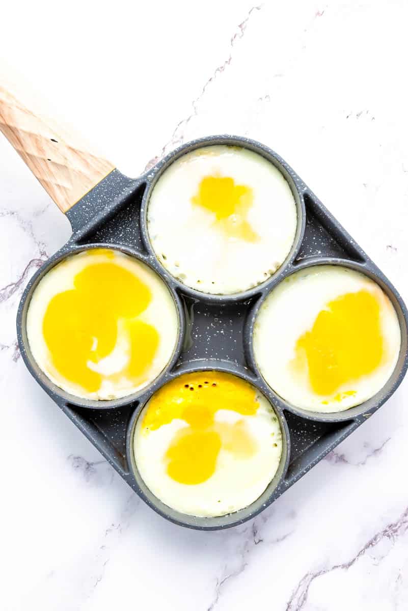 Four egg cups with cracked eggs in gray pan on white background.