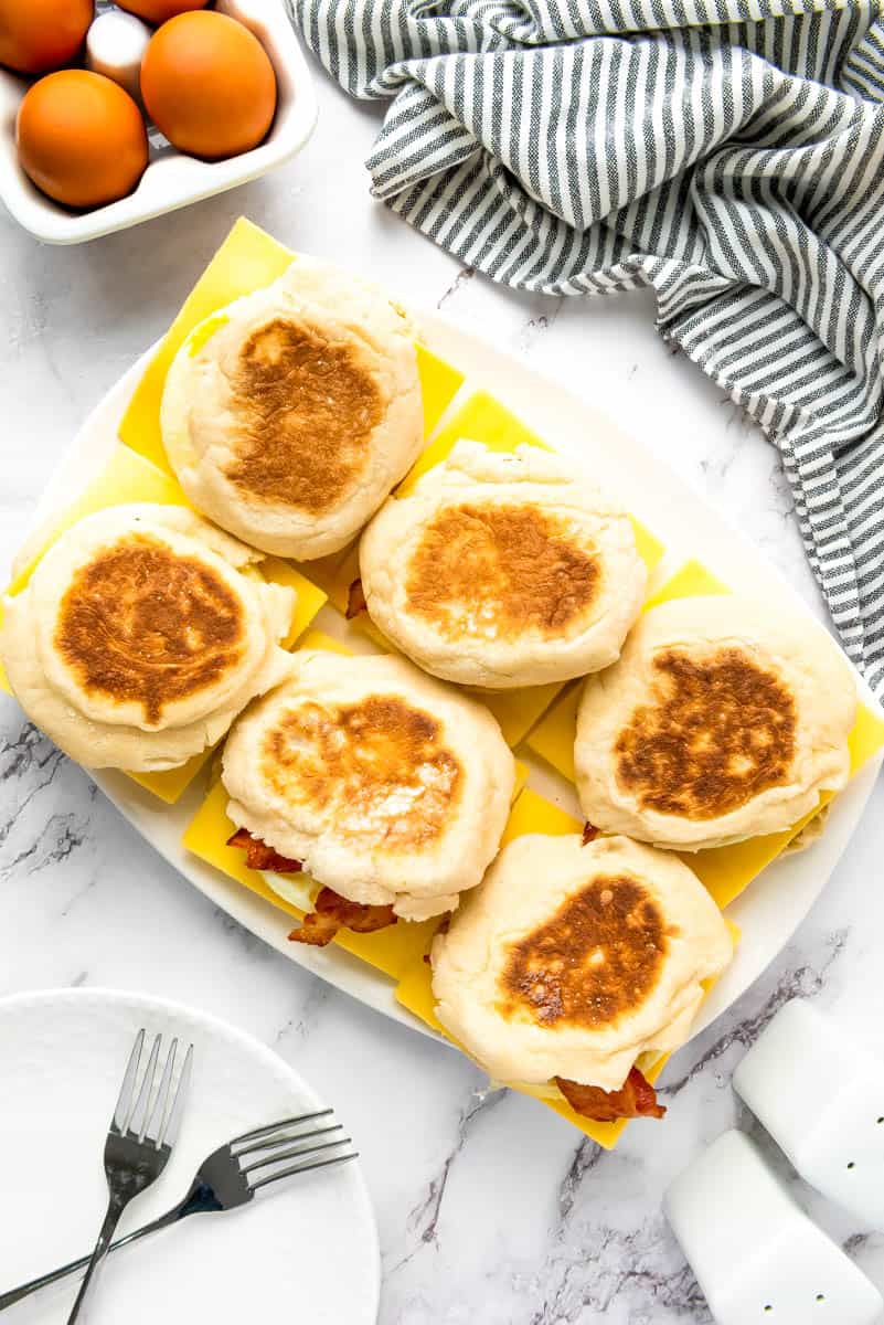 Plate with six breakfast sandwiches on white background and stripe towel above.