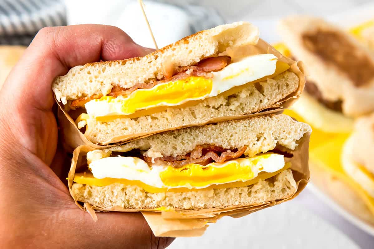 Hand holding a stacked breakfast sandwich against gray background.