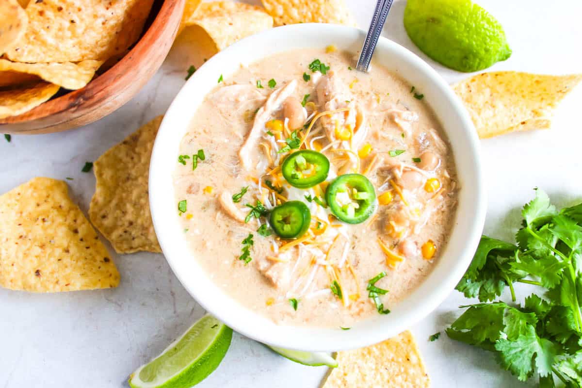 White bowl of white chicken chili with chips, lime wedge and cilantro surrounding.