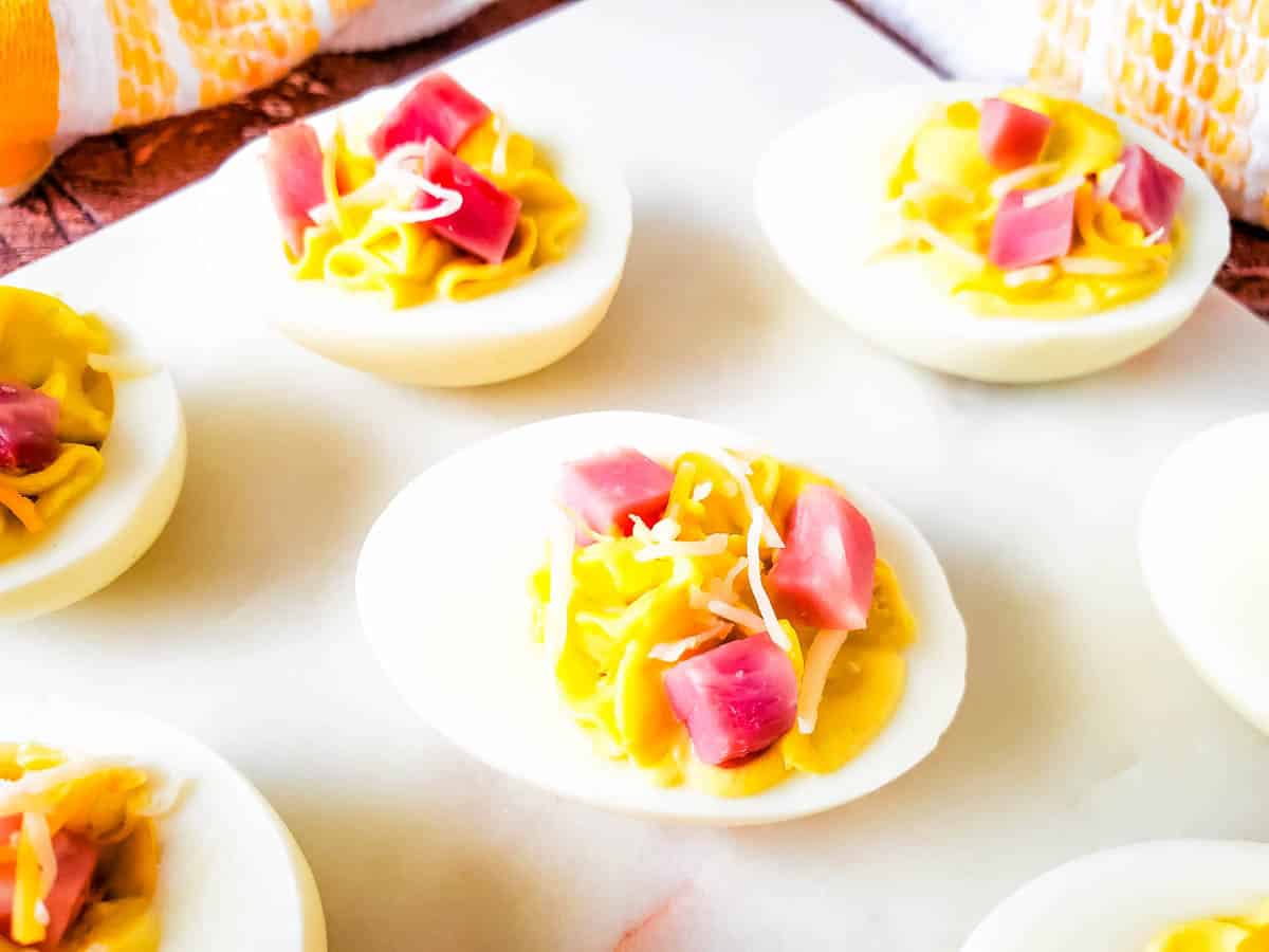Close up of several ham and cheese deviled eggs on white cutting board