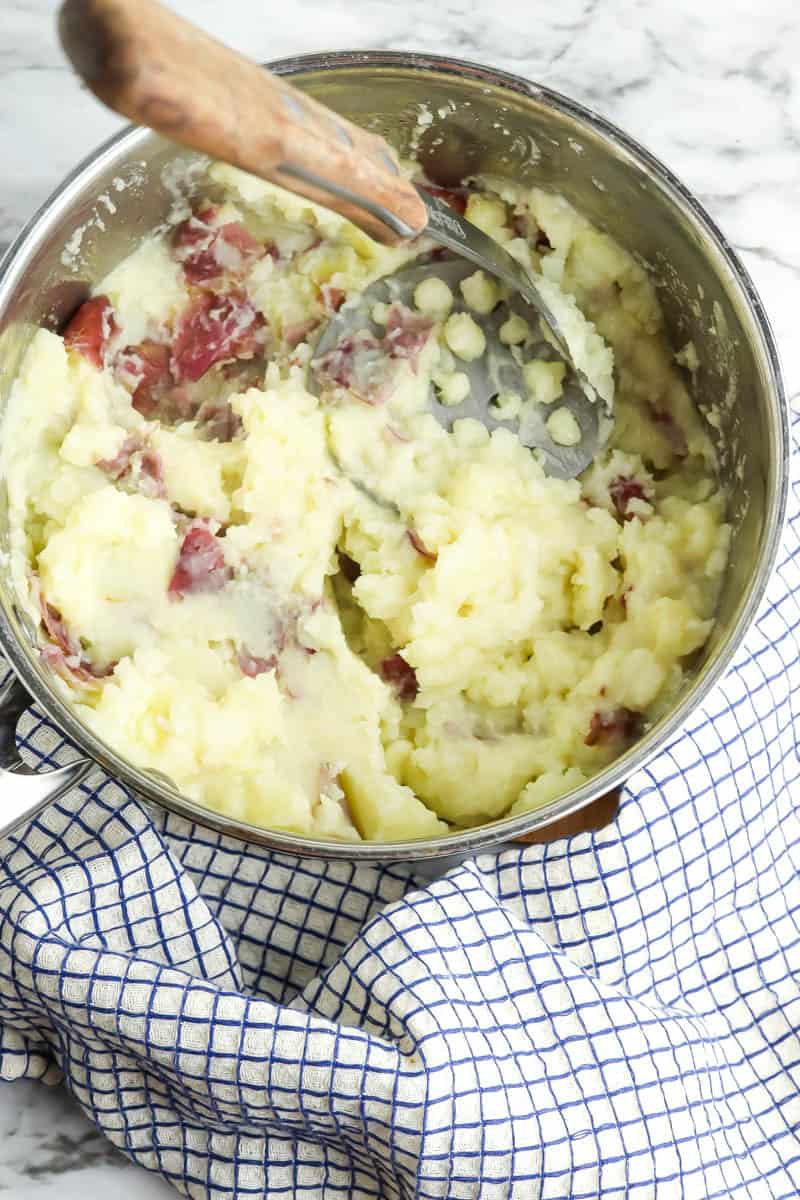 Pot of mashed potatoes being mashed with a potato masher after butter added.
