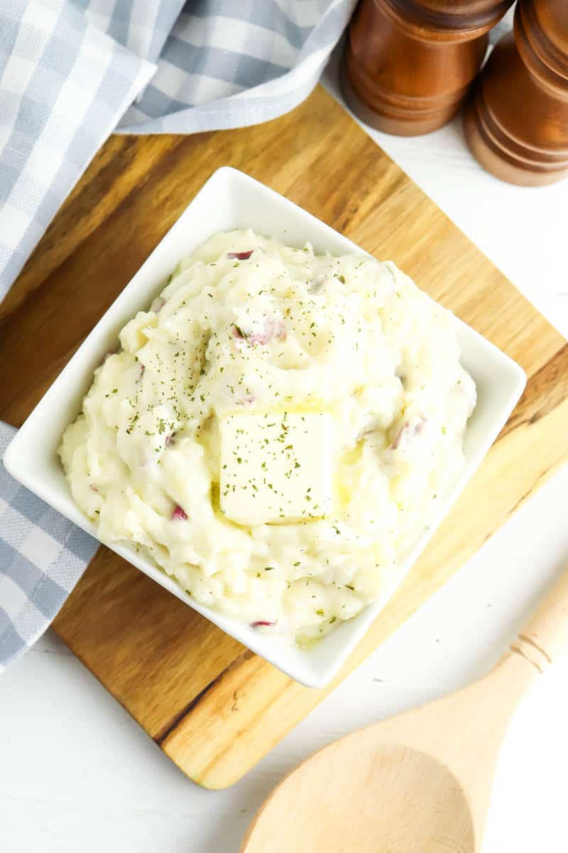 White bowl with mashed potatoes on wooden cutting board