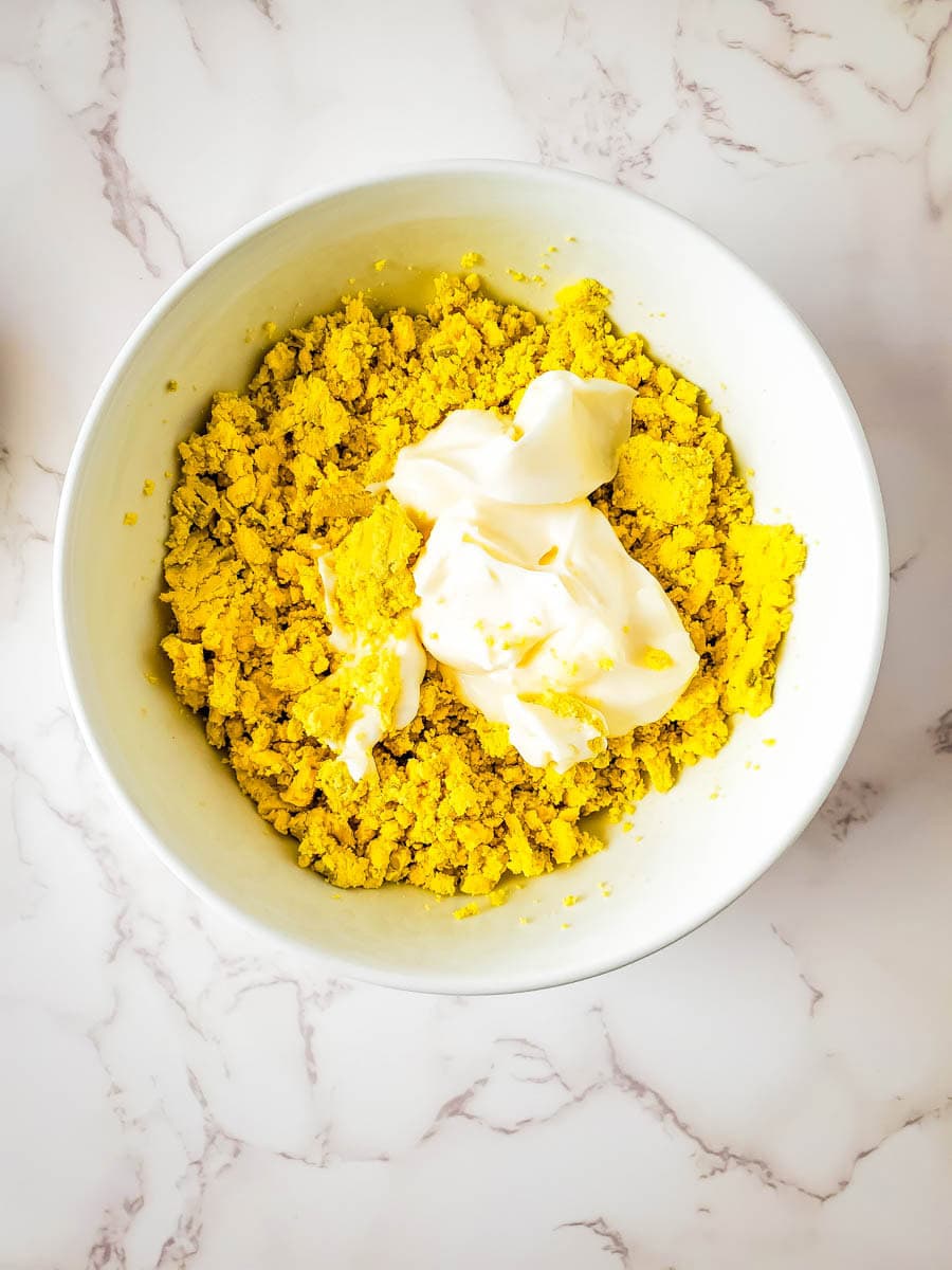 White bowl with mashed yellow egg yolks and mayo