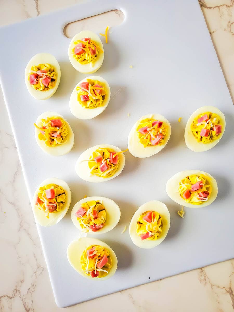 A dozen Ham and cheese deviled eggs on a white cutting board