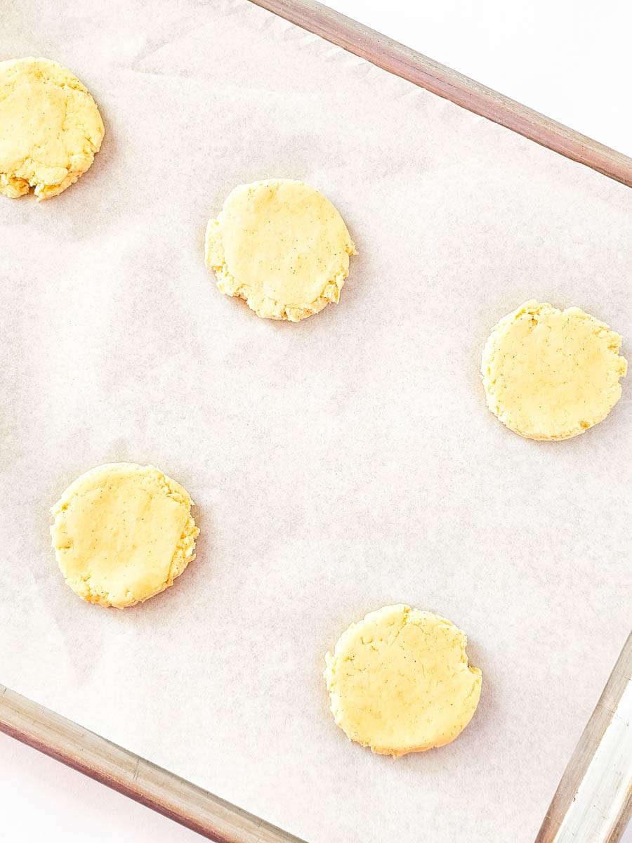 Flattened shortcakes on a sheet pan with parchment paper.