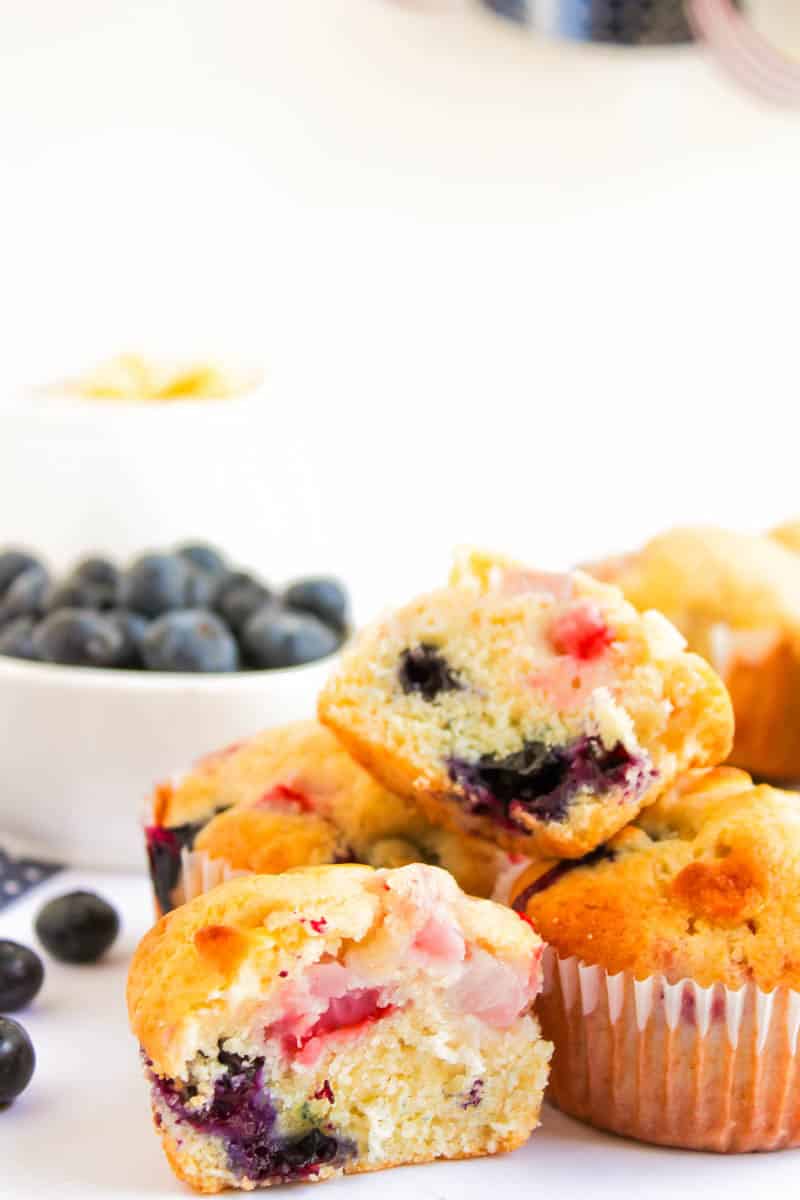 Stacked muffins with one cut open and blueberries in the back corner