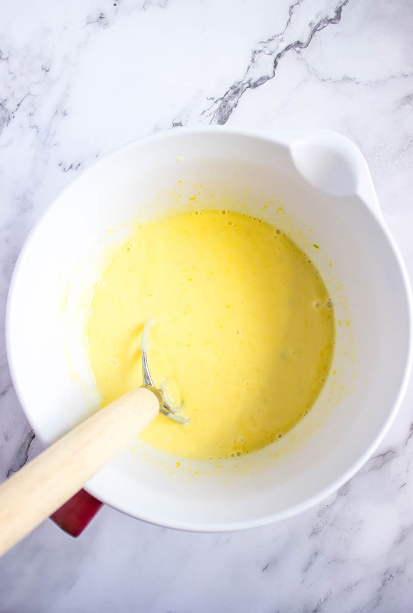 The mixture of sweetened condensed milk, egg yolks, key lime juice and zest in a mixing bowl with a spoon.