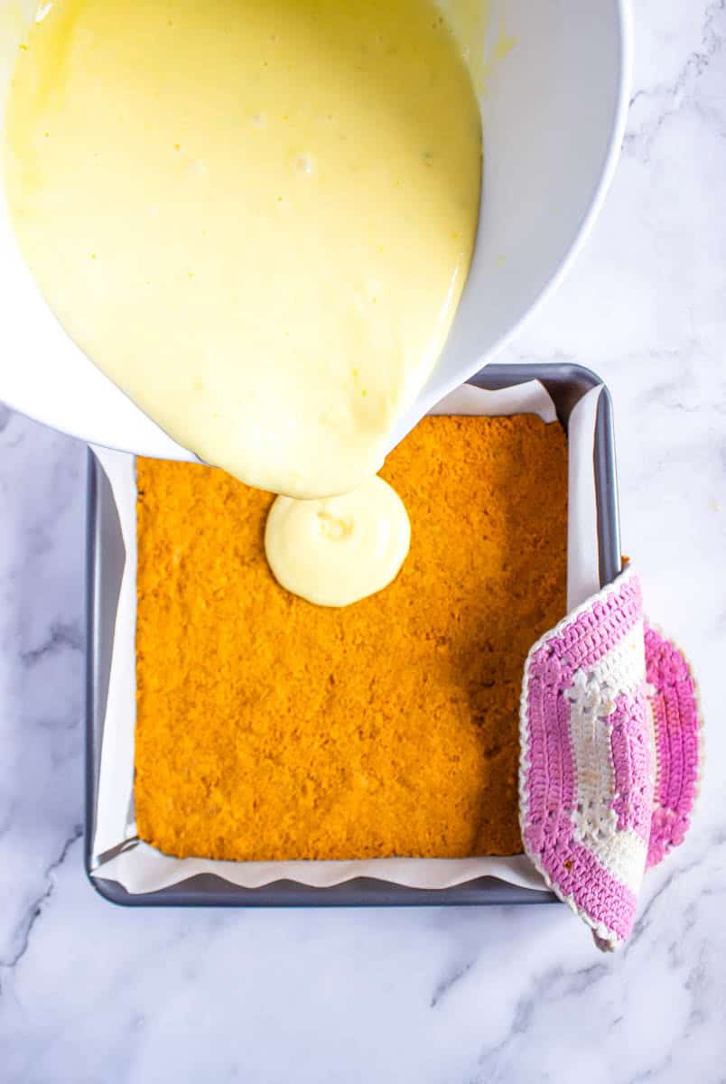 Pouring the sweetened condensed milk mixture over the graham cracker bar crust.