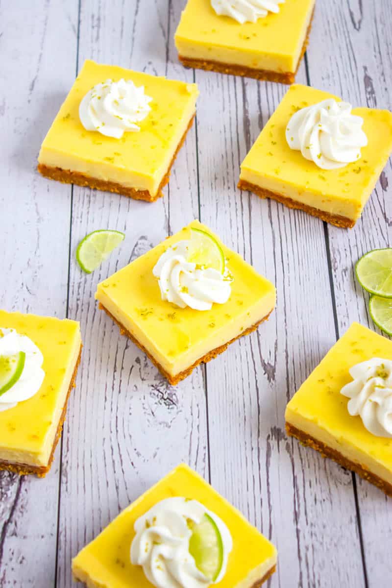 Several key lime pie bars on a wooden background topped with whipped cream and lime zest.