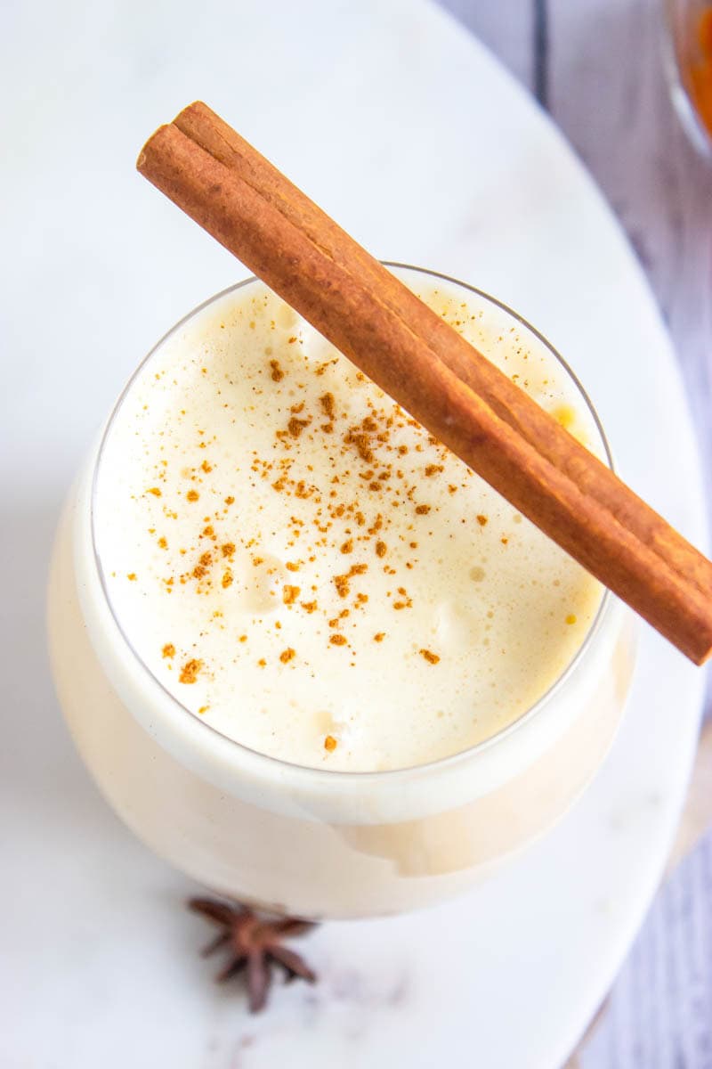 A glass of pumpkin spice eggnog overhead with a cinnamon stick on top
