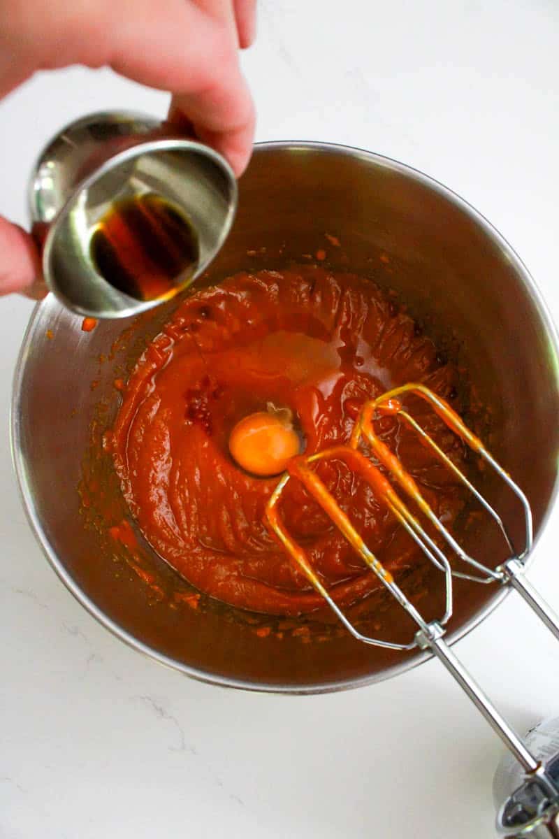 Bowl with the sugars, pumpkin puree, butter being mixed with the egg and vanilla extract being poured in.