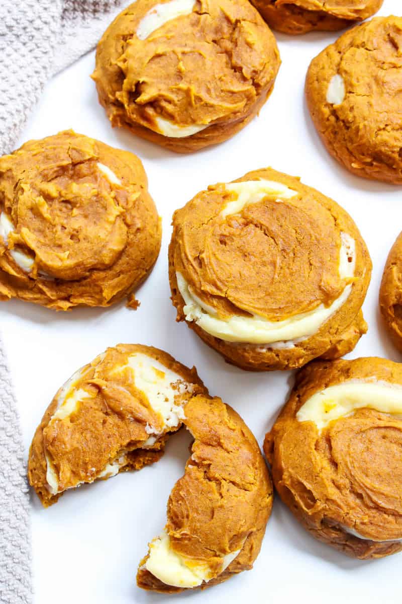 Pumpkin cheesecake cookies on white background with one cut in half.