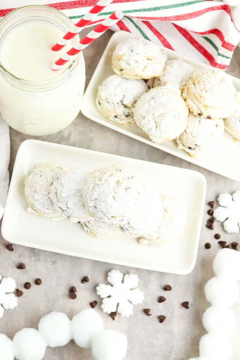 Gluten free snowball cookies on white plate and white serving plate with a glass of milk beside them.