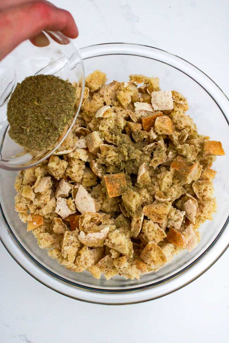 Sprinkling seasonings over dried bread cubes in a bowl.