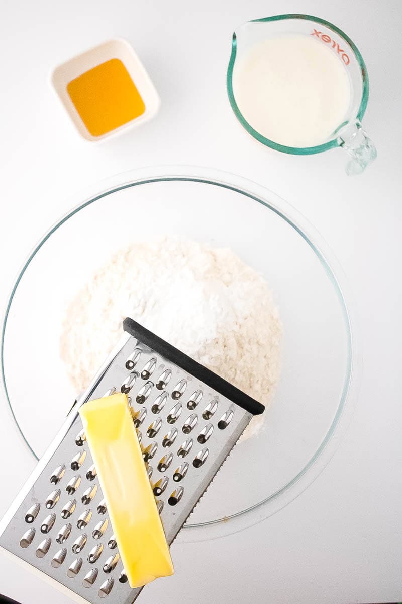 Bowl with flour and a grater with a stick of butter overtop with bowl of honey in corner